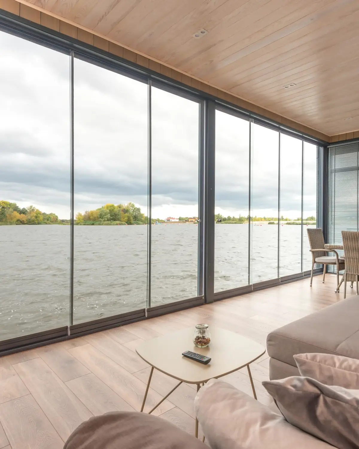 A living room with floor to ceiling glass walls looking out over calm water